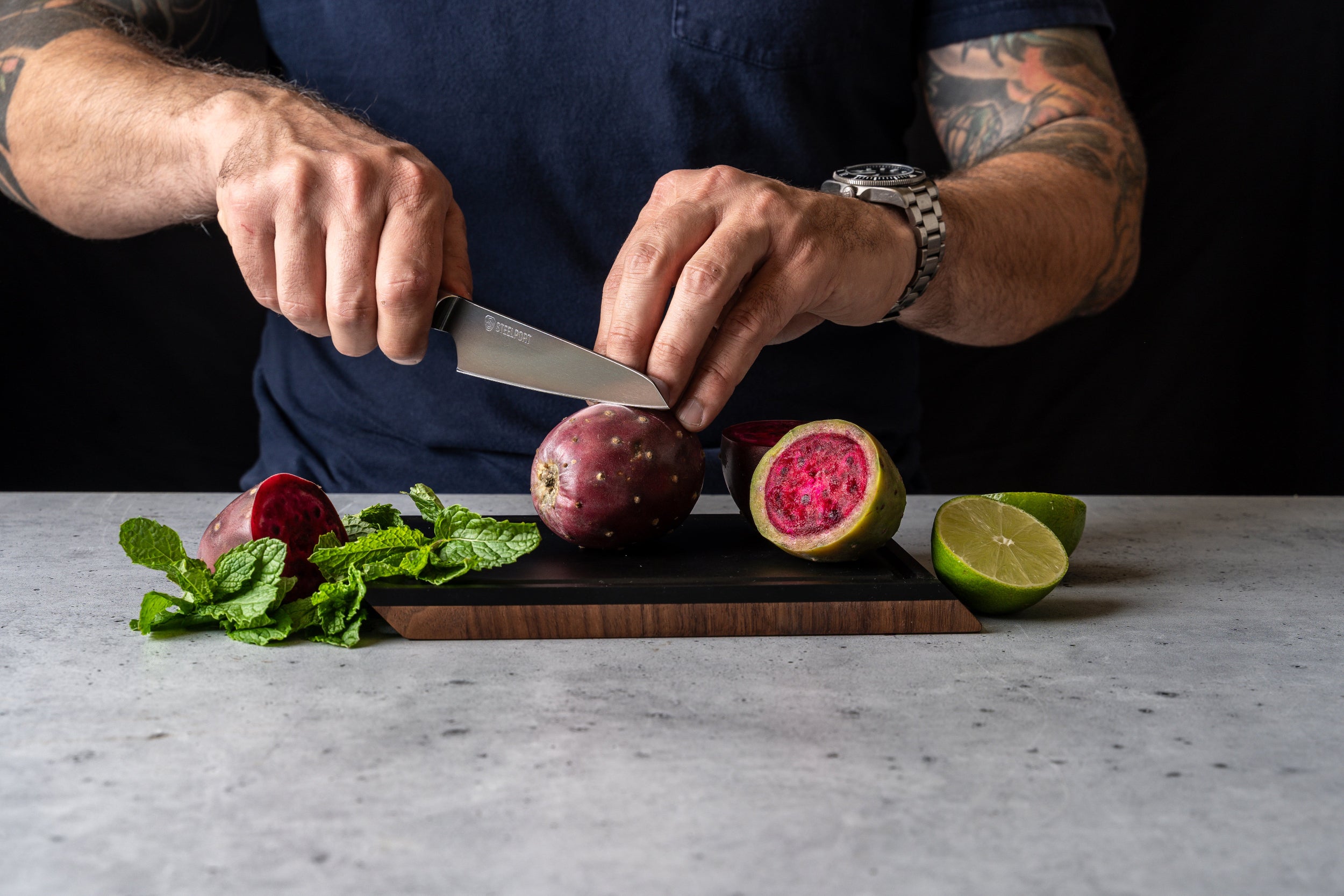 Person cutting a watermelon radish on a SteelCore™ cutting board with a STEELPORT Paring knife, surrounded by fresh herbs and a lime.